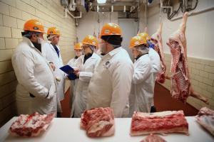 group of people in white coats and orange hard hats judging raw meat