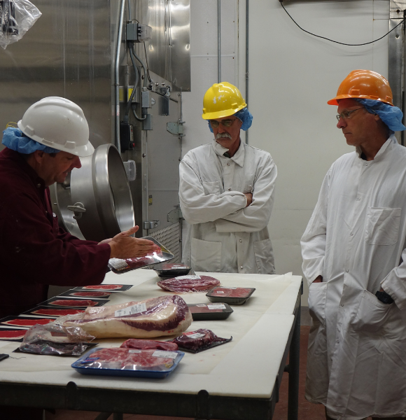 4 men in hard hats with packaged meat on table