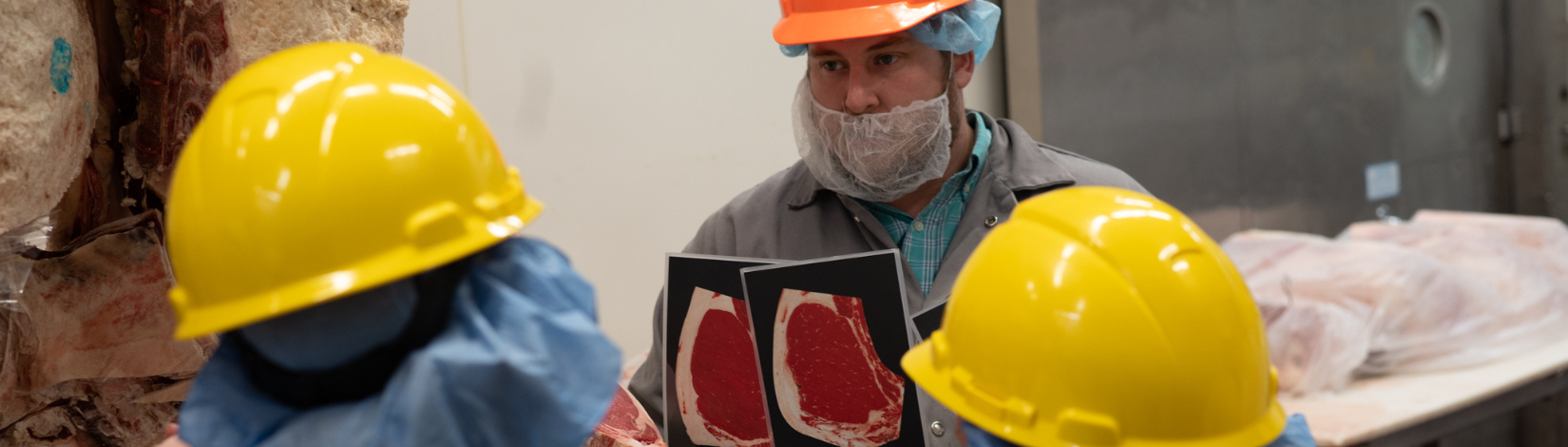 Instructor in hard hat holding up images of beef cuts