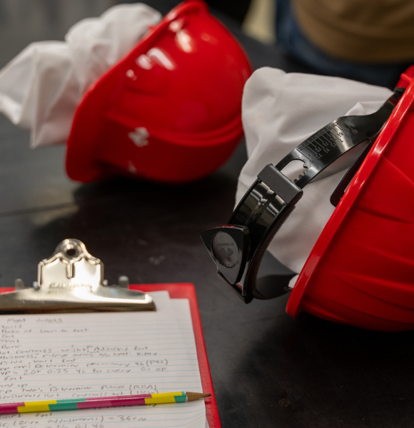Two red hard hats on table next to note pad
